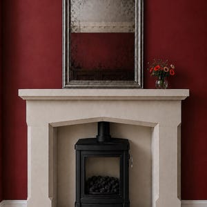 May include: A light beige stone fireplace surround featuring a rectangular opening, housing a black metal wood-burning stove with a glass door. Above the mantel sits a tall, arched, silver-framed mirror with a distressed, antique-style glass finish.
