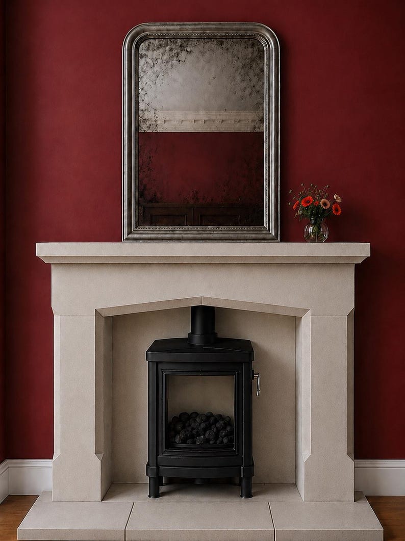 May include: A light beige stone fireplace surround featuring a rectangular opening, housing a black metal wood-burning stove with a glass door. Above the mantel sits a tall, arched, silver-framed mirror with a distressed, antique-style glass finish.