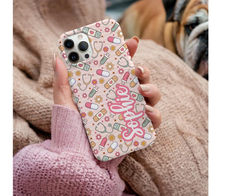 May include: A pink phone case featuring a pattern of medical symbols, including stethoscopes, bandages, pills, and syringes. The name "Sophie" is written in cursive script. The case is designed for a smartphone.