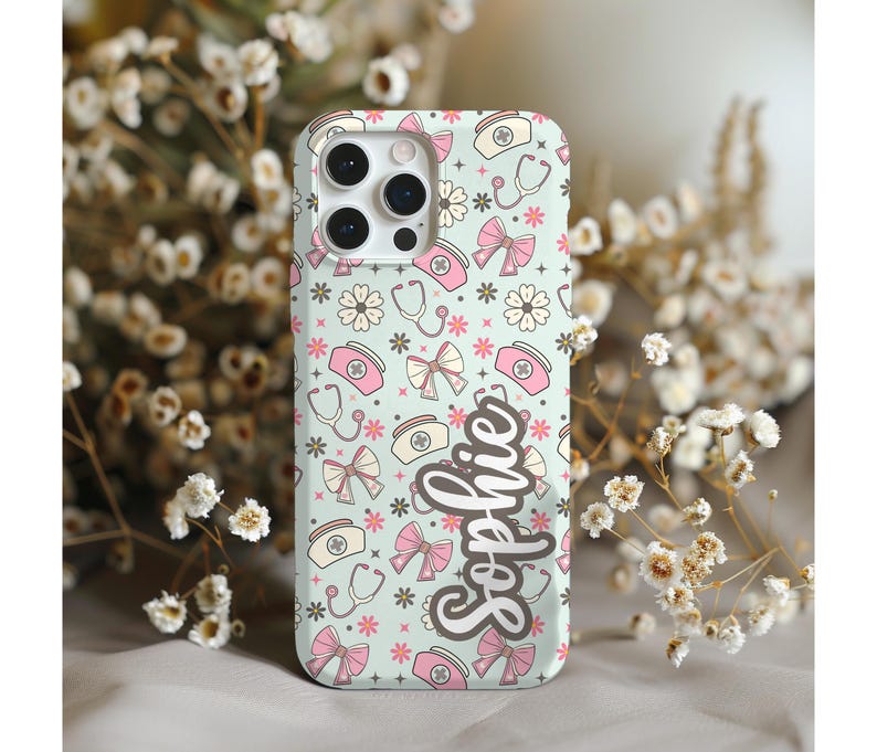 May include: A light green phone case with a pattern of pink bows, nurse hats, stethoscopes, and flowers. The name "Sophie" is written in cursive. The case has a camera cutout and is surrounded by white flowers.