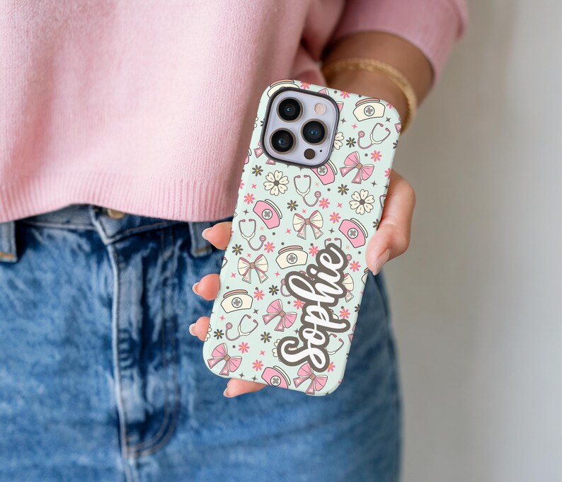 May include: A light blue phone case with a pattern of medical symbols, bows, and flowers in pink and white. The name "Sophie" is written in a cursive font on the case.