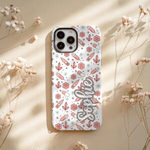 May include: A white phone case with a pattern of pink flowers, syringes, pills, and leaves. The name "Sophie" is written in cursive on the side. The case has a camera cutout.