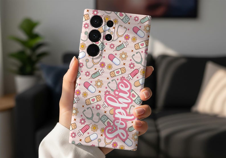 May include: A phone case with a repeating pattern of medical-themed illustrations, including stethoscopes, pills, syringes, and bandages, in pastel colors. The name "Sophie" is written in a cursive font. The case has a pink background.