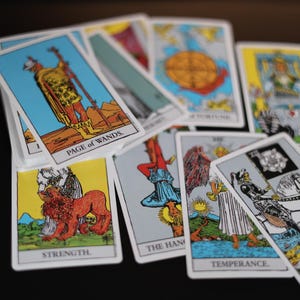 May include: A collection of tarot cards, featuring illustrations and titles such as "Page of Wands," "Strength," and "Death." The cards have white borders and colorful imagery, including figures, symbols, and scenes.