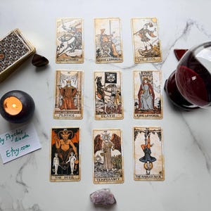 May include: A tarot card reading setup with a deck of cards, a lit candle, a crystal ball, and individual tarot cards. The cards display illustrations and symbols, with the text "By Psychic Wanda Etsy.com" on a small note.