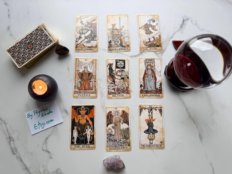 May include: A tarot card reading setup with a deck of cards, a lit candle, a crystal ball, and individual tarot cards. The cards display illustrations and symbols, with the text "By Psychic Wanda Etsy.com" on a small note.