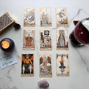 May include: A tarot card reading setup featuring a deck of cards, a lit candle, a crystal ball, and several individual tarot cards. The cards depict various illustrations and symbols, with a handwritten note in the corner.