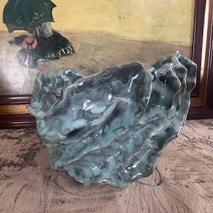 May include: A ceramic bowl with a unique, textured design. The bowl features a wavy, layered pattern with a glossy, teal and dark blue glaze. The bowl is a decorative piece.