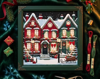 Op de afbeelding: Een ingelijste kruissteek met een besneeuwde kerstdorp-scène met rode en groene huizen, verlichte ramen en feestelijke versieringen. De groene lijst heeft gouden hoekaccenten. Cadeaus, groen en borduurgaren omringen het frame.