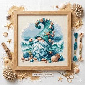 May include: Cross-stitch artwork of a gnome with a long white beard and a teal hat decorated with seashells and starfish. The gnome is set against a backdrop of ocean waves. The framed artwork is surrounded by sand, seashells, and embroidery floss.