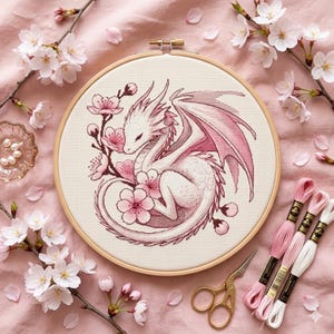 May include: A cross-stitch embroidery of a white dragon with pink wings and cherry blossoms in a wooden hoop. The dragon is surrounded by pink flowers and branches, with pink embroidery threads and gold scissors.