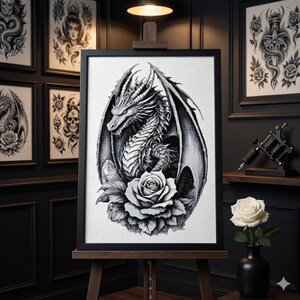 May include: Black and white framed artwork of a dragon with large wings and a rose. The dragon is the focal point, with intricate details. The artwork is displayed on a wooden easel, with other framed art in the background.