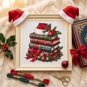May include: A framed cross-stitch design depicts a stack of books adorned with a Santa hat, holly, and ornaments. Two miniature Santa hats sit above the frame. Red and green embroidery floss, scissors, and a decorative book with a red bow are also present.