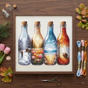 May include: A framed cross-stitch embroidery depicting four glass bottles, each containing a different seasonal landscape: a snowy winter scene, a spring tulip garden, a sunny summer beach, and an autumn forest with falling leaves.