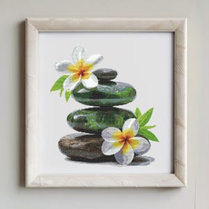 May include: A stack of smooth gray stones with white and yellow flowers on top. The stones are arranged in a zen garden style.