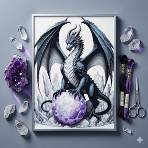 May include: A framed cross-stitch of a blue dragon with large wings, perched on a purple orb. The dragon has a detailed design, with a white chest and red eyes. The image is surrounded by crystals and embroidery supplies.