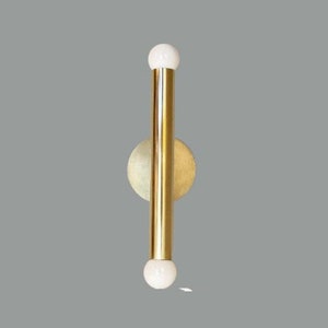 May include: A gold wall sconce with two white globe light fixtures. The sconce has a round base and a long, thin, cylindrical stem.