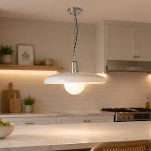 Op de afbeelding: Een hanglamp met een brede, ondiepe, witte metalen kap en een centrale bol van matglas. De lamp hangt aan een zilverkleurige ketting en armatuur en zorgt voor neerwaartse verlichting boven het oppervlak van een keukeneiland.