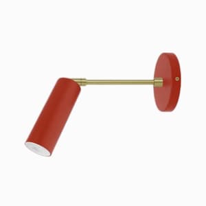 May include: A red wall-mounted light fixture with a cylindrical shade and a brass arm. The light fixture is mounted to a round base.