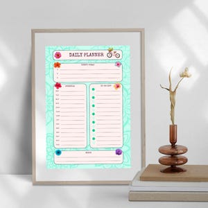 May include: A turquoise and pink daily planner with a floral design. The planner has sections for today's goals, schedule, to-do list, and notes. A bicycle with flowers in the basket is at the top of the planner.