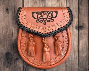 May include: A brown leather sporran with a black braided trim and a Celtic knot design. The sporran has three tassels.