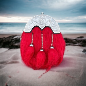 May include: A red kilt sporran with silver accents and a thistle design. The sporran has three tassels and is made of a soft, fuzzy material.