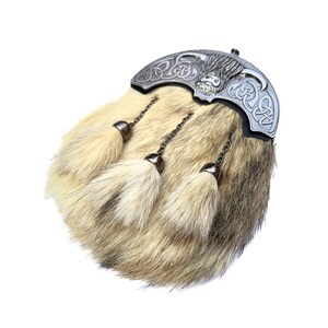 Op de afbeelding: Een sporran van bruin en wit bont met een zilveren metalen versiering met een Keltisch knoopontwerp en een Highland-koeienkop. De sporran heeft drie kwastjes.