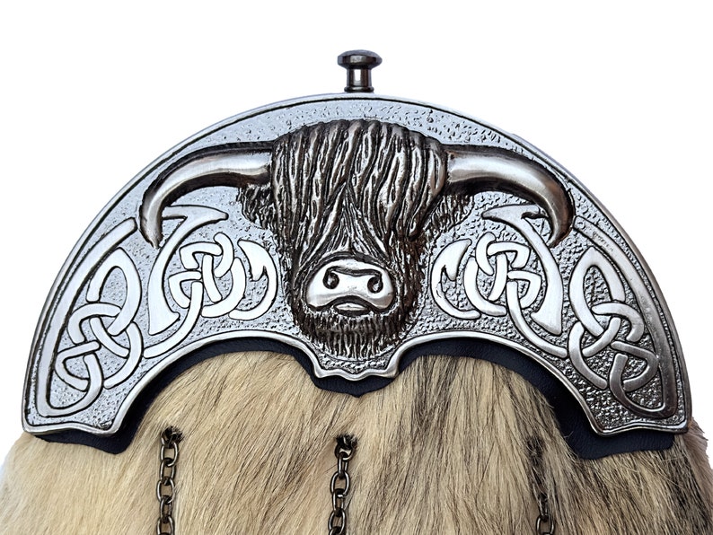 Op de afbeelding: Een zilveren kiltpin met een Hooglandkoe-ontwerp en Keltische knoopwerk. De pin is bevestigd aan een ketting.