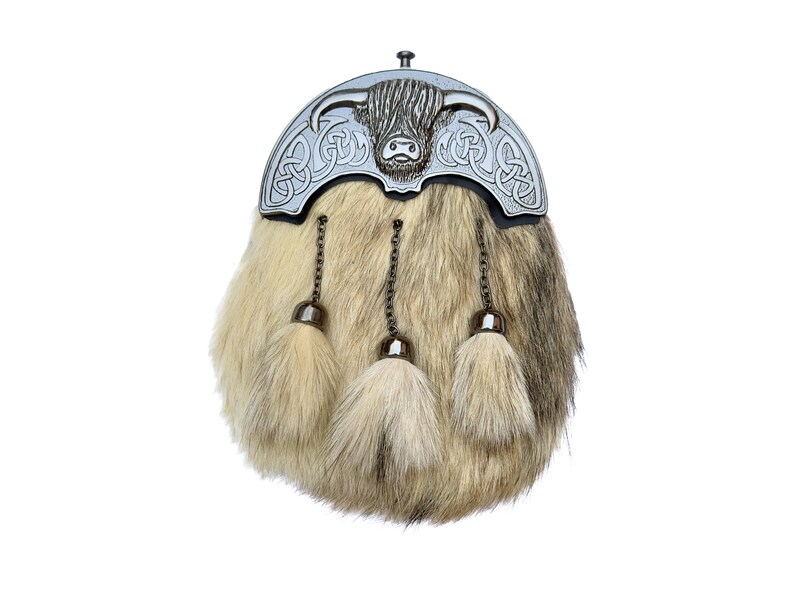 Op de afbeelding: Een zilveren kiltpin met een Hooglandkoe-ontwerp en Keltische knoopwerk. De pin is bevestigd aan een sporran van bruin en wit bont met drie kwastjes.
