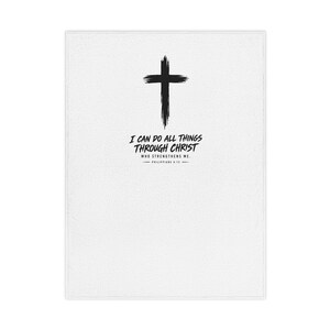 Op de afbeelding: Een witte rechthoekige deken met een zwart kruis in penseelstreekstijl, gecentreerd aan de bovenkant. Onder het kruis staat de tekst: I CAN DO ALL THINGS THROUGH CHRIST WHO STRENGTHENS ME. PHILIPPIANS 4:13, gedrukt in een vetgedrukt zwart lettertype.