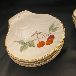 May include: Set of four white ceramic shell-shaped serving dishes with gold trim. One dish features a painted design of cherries on a branch, while the other features a painted design of oranges on a branch.