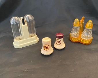 May include: Set of four vintage salt and pepper shakers. Two clear glass shakers in a yellow plastic holder. Two white plastic shakers with a red "TWA" logo.
