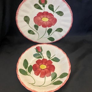May include: Two white ceramic bowls with a red floral design. Each bowl features a large red flower with a yellow center, green leaves, and a red rim. The bowls are likely for serving or display.