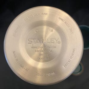 May include: Bottom view of a stainless steel Stanley water bottle. The base includes the text "DO NOT MICROWAVE", "HAND WASH ONLY", "BPA FREE", and "25 oz / 750 mL". The bottle is made in China.