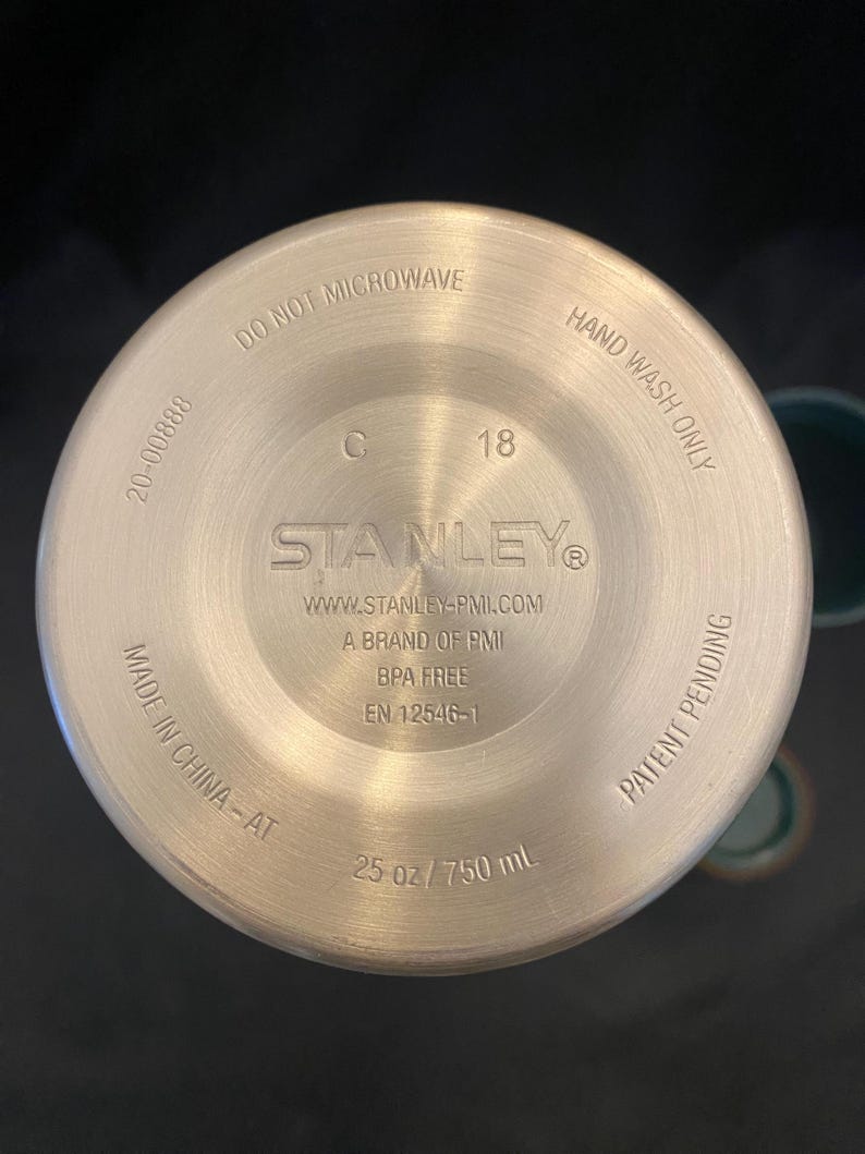May include: Bottom view of a stainless steel Stanley water bottle. The base includes the text "DO NOT MICROWAVE", "HAND WASH ONLY", "BPA FREE", and "25 oz / 750 mL". The bottle is made in China.