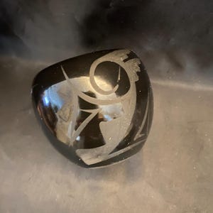 May include: A black, rounded, decorative object with a glossy finish. The surface features an etched, abstract design in a lighter color, creating a contrast. The object's shape is smooth and curved, with a reflective quality.