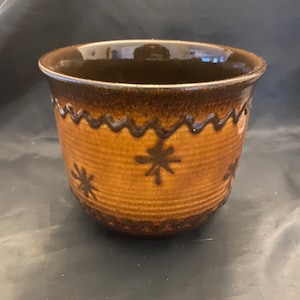 May include: A brown ceramic planter with a wavy brown rim and a brown glaze. The planter has a pattern of brown stars on the front.