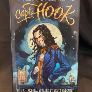 May include: Book cover featuring a young boy with dark hair and a blue jacket. The title of the book is "Capt. Hook" and the subtitle is "The Adventures of a Notorious Youth". The book is illustrated by Brett Helquist.