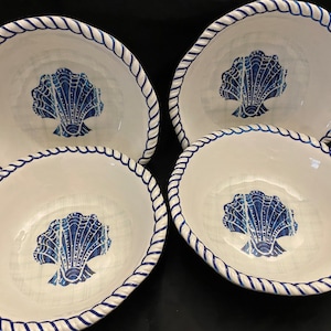 May include: Four white ceramic bowls with a blue seashell design in the center. Each bowl has a blue rope-like border. The bowls are oval-shaped and are likely for serving food.