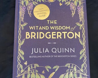 May include: A purple hardcover book titled The Wit and Wisdom of Bridgerton by Julia Quinn. The cover features gold foil illustrations of vines, leaves, and bees, with a circular gold emblem reading Lady Whistledown's Official Guide.