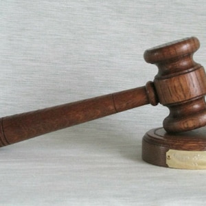 May include: A wooden gavel with a brown handle and a dark brown base. The base has a brass plaque with the inscription "Judge's Gavel".