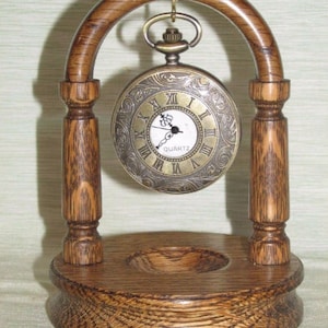 Peut inclure: Un support en bois avec une arche incurvée pour exposer une montre de poche. Le support est en bois foncé avec un motif de grain. La montre de poche est dorée avec des chiffres romains et un cadran blanc. Le cadran de la montre indique "QUARTZ".