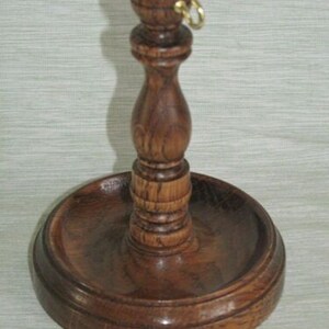 May include: A handcrafted wooden candle holder with a dark brown finish. The holder features a round base, a central stem, and a small ring at the top. The design is classic and elegant, suitable for various home decor styles.