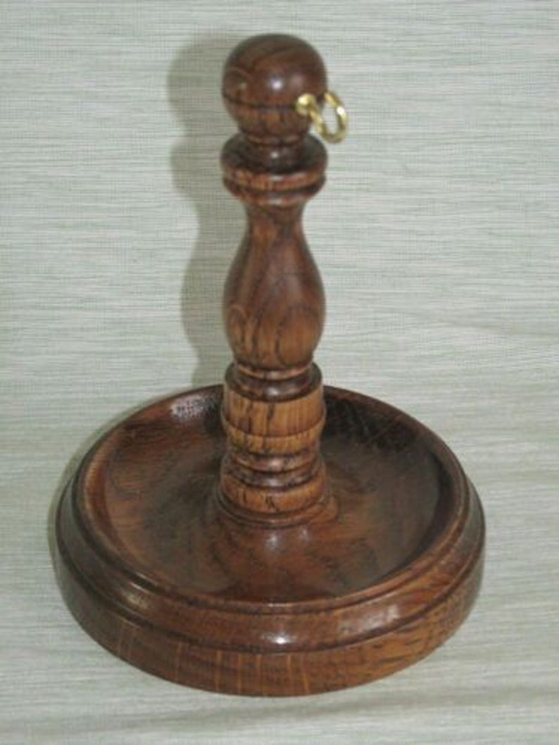 May include: A handcrafted wooden candle holder with a dark brown finish. The holder features a round base, a central stem, and a small ring at the top. The design is classic and elegant, suitable for various home decor styles.