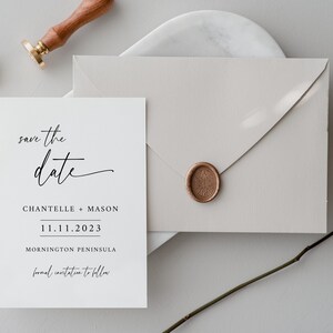 May include: A minimalist wedding invitation suite featuring a white card with "save the date" script, names, and date. A light gray envelope with a wax seal and a dried rose are also present. A wooden stamp is visible.