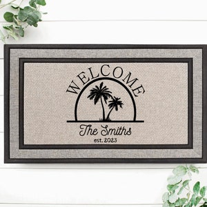 May include: A welcome mat with a black and white design of palm trees and the text "WELCOME The Smiths est. 2023". The mat has a gray and black border.