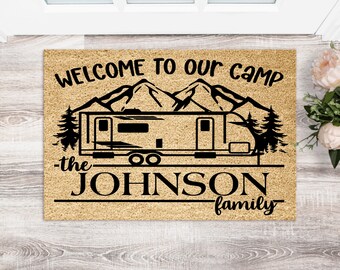 May include: Welcome to our camp doormat with a black silhouette of a camper, mountains, and trees. The text "the JOHNSON family" is below the camper.