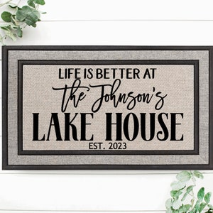 May include: A gray doormat with black text that reads "Life is better at the Johnson's Lake House Est. 2023". The doormat has a black frame.