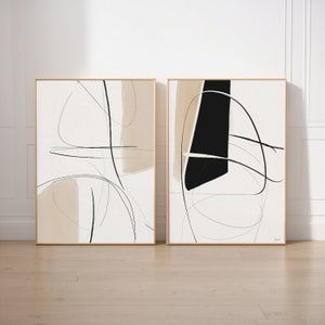 Puede incluir: Un conjunto de dos impresiones de arte abstracto con líneas negras y formas beige sobre un fondo blanco. Las impresiones están enmarcadas en madera natural.
