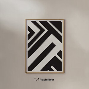 May include: Geometric black and white art print in a gold frame. The artwork features a bold, abstract design of intersecting lines and shapes. The print is displayed on a neutral-colored wall, creating a modern aesthetic.